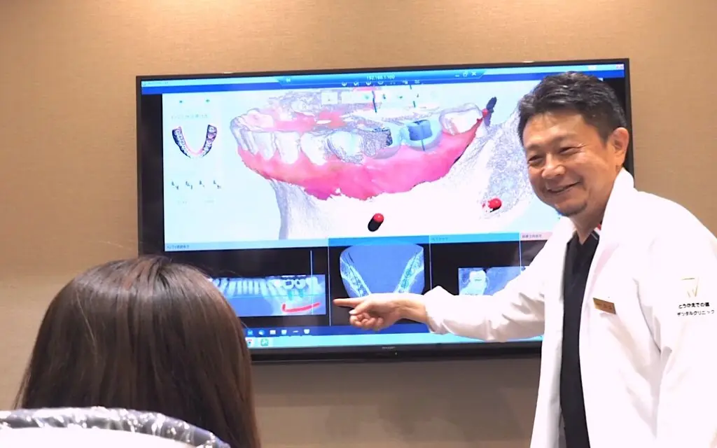 大型モニターに3Dの顎骨画像を映して患者に説明する歯科医師
